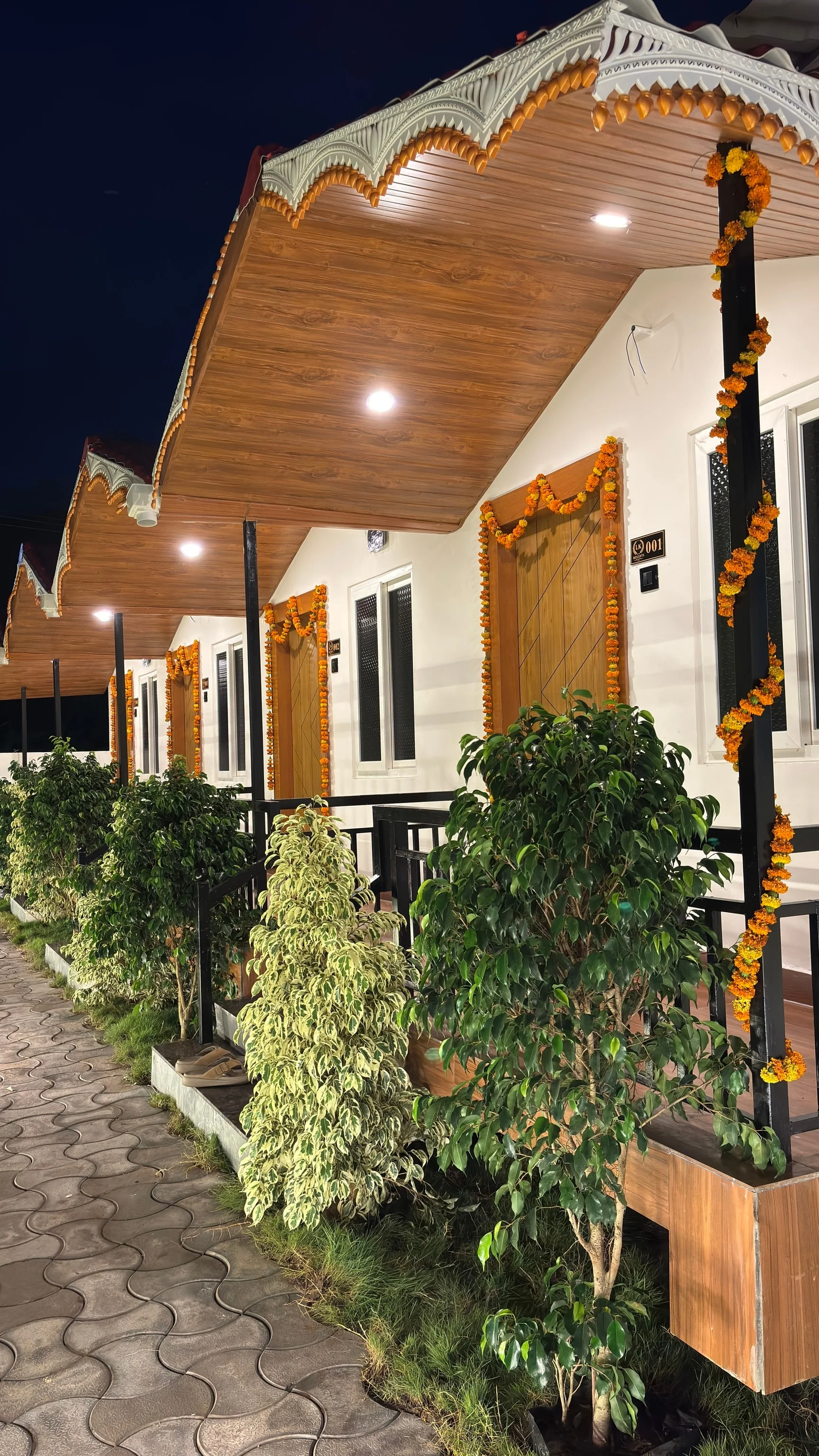 Mẫu nhà 2 tầng đẹp với mái hiên gỗ trang trí hoa cúc vàng và cây xanh vào ban đêm